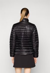 Sort pufferjakke med horisontal quiltet design, høj krave og glat, blank overflade. Har en diskret lomme på bagsiden.