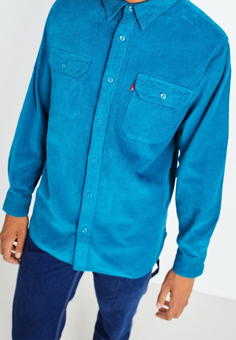 Camicia in corduroy turchese con maniche lunghe, colletto a bottoni, due tasche sul petto e bottoni a contrasto. Tessuto in cotone con una finitura morbida.