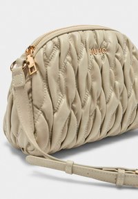 Beige gesteppte Handtasche mit Reißverschluss, ausgestattet mit einem abnehmbaren Schultergurt und goldfarbenen Beschlägen. Weiche Textur mit subtilen Stickdetails.