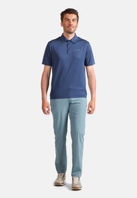 Mörkblå pikétröja för män med krage, som är kombinerad med ljusblå slim-fit byxor och beige sportskor. Tröjan har en logotyp på vänster sida.