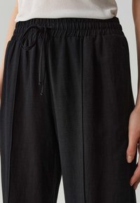 Schwarze, leichte Leinenmischungshosen mit elastischem Bund und Kordelzug, die eine entspannte Passform und eine glatte Textur bieten.