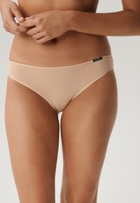 Beżowe majtki bikini z mieszanki bawełny o gładkiej fakturze, niskim kroju oraz małą czarną metką na pasku.