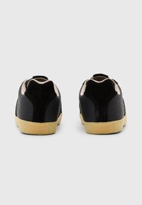 Baskets noires avec cuir texturé, accents en daim et une semelle intermédiaire crème. Présente une étiquette logo en or au niveau du talon.