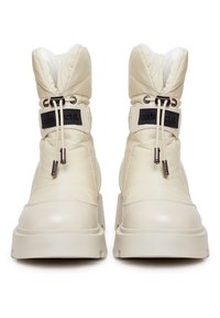 Botas de invierno blancas acolchadas con caña alta, que presentan herrajes negros y un parche con el logo. Materiales suaves y texturizados se combinan para un aspecto único.
