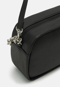 Czarna skórzana torebka w kształcie prostokąta, z zamkiem błyskawicznym i łańcuszkiem jako akcentem na pasku. Gładka tekstura, minimalistyczny design.