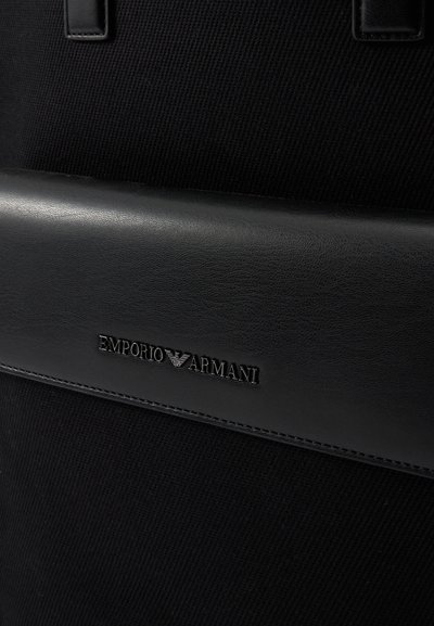 Melna auduma soma ar gludu melna ādas akcentu, iegravētu "Emporio Armani" logo un teksturētu materiālu kontrastam.