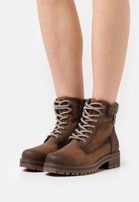 Brown lace-up ankle boots featuring a textured upper, metallic eyelets, and a knit collar. Sturdy rubber sole with a tread pattern.