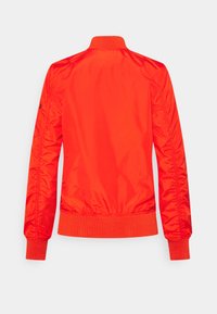 Röd nylonjacket med bomberstil, ribbad krage och mudd. Slät textur, figursydd midja och rynkningar vid ärmsömmarna för en strukturerad look.