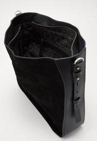 Svart mocka- och läderhandväska med en bred öppning, innerväska med dragkedja och signaturmönstrad foder. Justerbar axelrem ingår.