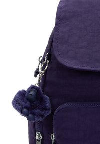 Lila ryggsäck med en matchande fluffig gorillanyckelring fäst vid en silverdragkedja på sidofickan.