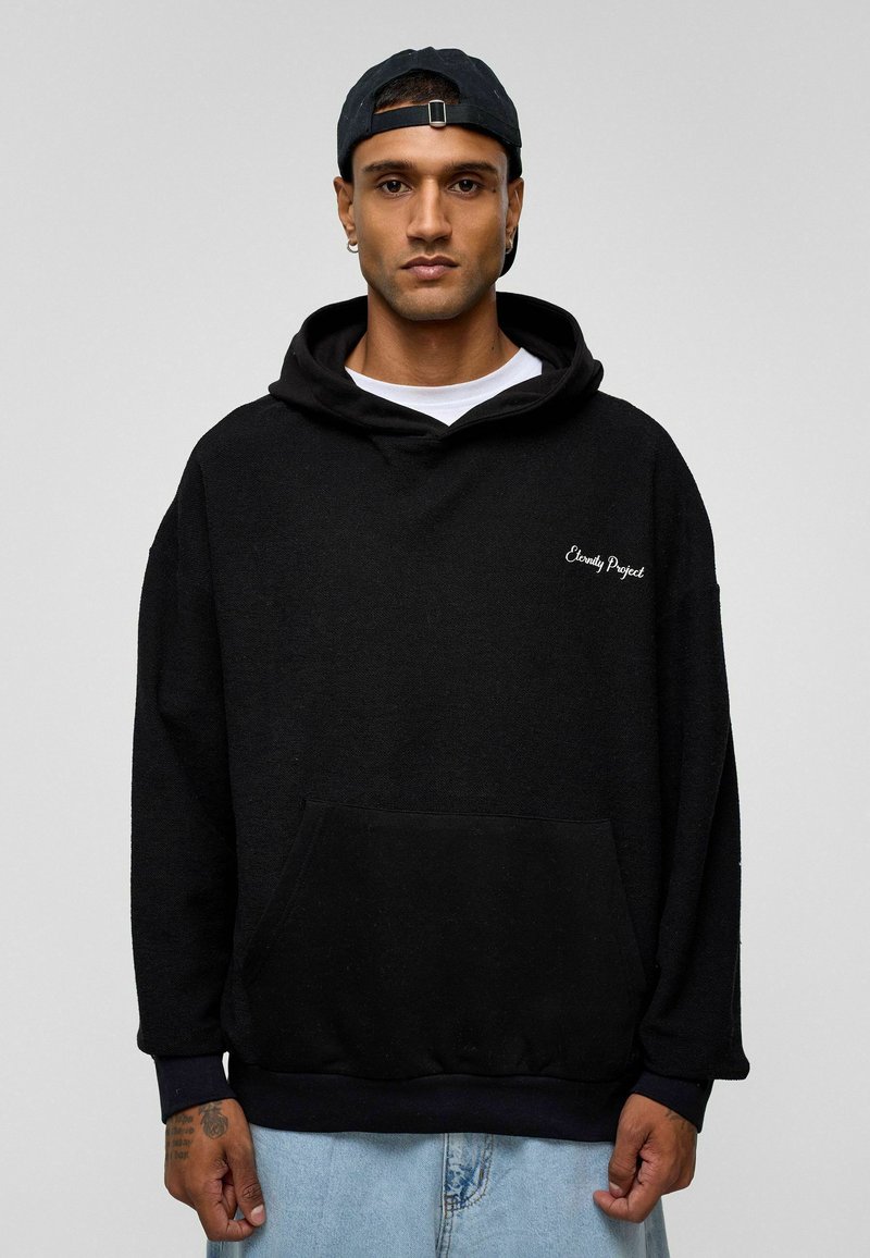 Sweatshirt à capuche noir avec poche kangourou, poignets élastiques et texte brodé "Eternity Project" sur la poitrine. Tissu en mélange de coton.