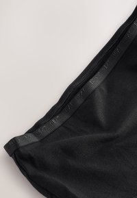 Indumento in tessuto nero con una texture liscia ed elastica e una leggera lucentezza. Include una fascia in vita nera elegante con marchio in rilievo.