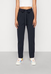Pantalons taille haute navy avec une ceinture nouée, dotés de plis, de jambes fuselées et d'une texture lisse, associés à des baskets multicolores.