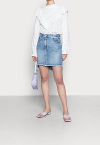 Vit texturerad blus med volangkrage, kombinerad med en ljusblå denimkjol. Tillbehören inkluderar en lavendelfärgad handväska och platta sandaler.