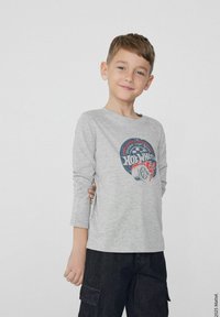 Šedé tričko s dlouhým rukávem, na kterém je barevný grafický design s textem "Hot Wheels" a ilustrací pneumatik, kombinované s tmavými cargo kalhotami.