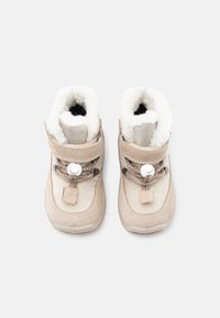 Bocanci de iarnă bej cu o căptușeală moale din fleece alb, formă rotundă, sistem de închidere cu șireturi ajustabile și accente din suede la gleznă.