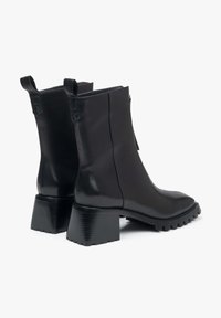 Black leather ankle boots with a chunky block heel, side zipper, and textured rubber sole. Features looped pull tabs at the back.