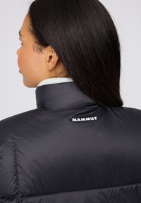 Schwarze Daunenjacke mit hohem Kragen und weißem "MAMMUT" Logo auf dem Rücken. Glatte Textur, minimalistisches Design und warme Fütterung.