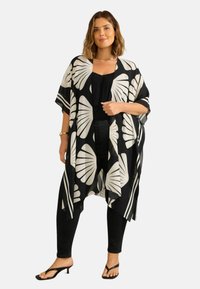 Mustakuvioinen kimono, jossa on suuria lehtikuvioita, kevyt kangas, avoin etuosa ja lyhyet hihat, kerroksittain mustan topin ja mustien farkkujen päällä.