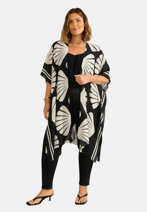 Mustakuvioinen kimono, jossa on suuria lehtikuvioita, kevyt kangas, avoin etuosa ja lyhyet hihat, kerroksittain mustan topin ja mustien farkkujen päällä.