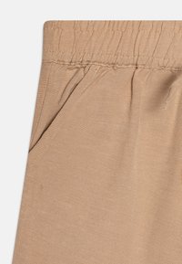 Pantalons beiges texturés avec une taille élastique et des poches latérales, fabriqués dans un tissu doux et respirant adapté à un usage décontracté.
