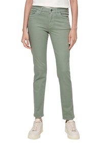 Jasnozielone, dopasowane dżinsy o gładkiej strukturze, pięć kieszeni i zapięcie na guzik, w połączeniu z beżowymi trampkami na masywnej podeszwie.
