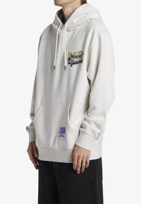 Jasnoszara bluza z kapturem wykonana z miękkiego materiału, wyposażona w przednią kieszeń, kaptur ze sznurkiem oraz wielokolorowe logo "DC Shoe Company" na piersi.