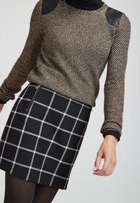 Suéter de punto en dorado y negro con hombros texturizados, combinado con una falda negra con un patrón de cuadrícula gris y detalle de cremallera lateral.