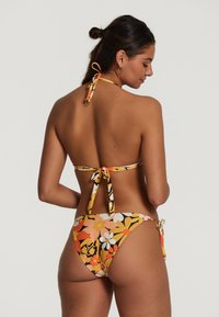 Virágmintás bikini szett narancssárga, sárga és fekete színekben. A felsőrész pántos, megkötős nyakkivágással rendelkezik; az alsórész oldalain szintén állítható megkötők találhatók.