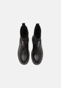 Bottines en cuir noir avec panneaux latéraux élastiques, bout rond et semelle en caoutchouc contrastante. Équipées d'une languette pour un enfilage facile.