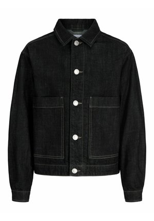 Junge steht, trägt schwarze Jeansjacke und weit geschnittene Jeans, weißes Hemd und beige Schuhe, schaut leicht nach rechts vor einfarbigem Hintergrund.