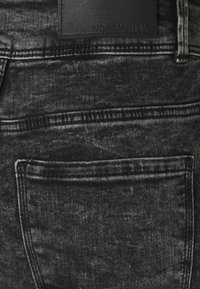 Pantalones vaqueros de mezclilla negros con efecto acid-wash, con un bolsillo trasero y costuras cosidas, además de una etiqueta de cuero negro con la inscripción "NOISY MAY" en la cinturilla.