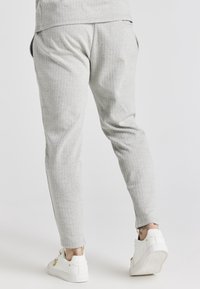 Světlé šedé kalhoty s rybí kostí vzorem a zúženým střihem, vybavené zipy na kotnících a bočními kapsami, doplněné bílými teniskami.