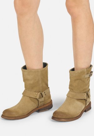 Stivaletti alla caviglia in suede beige con un aspetto leggermente consumato, dotati di una fascia avvolgente e dettaglio della fibbia, tacco in legno basso e punta arrotondata.