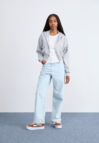 Grå zip-hoodie med en blød tekstur, hvid ribbet T-shirt, lyseblå vidde bukser og brune platform sneakers med hvide accenter.