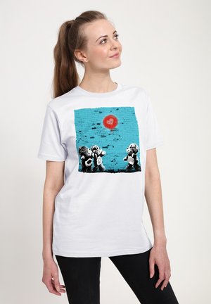 Hvid bomuld t-shirt med et grafisk motiv af to bamser mod en struktureret blå baggrund med en rød hjerteform over dem.