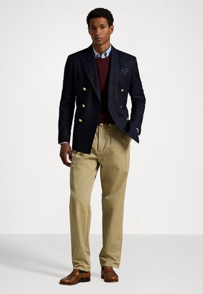 Blazer azul marino de doble botonadura con botones dorados, suéter burdeos, camisa azul claro, pantalones caqui y zapatos marrones. No se ven patrones.