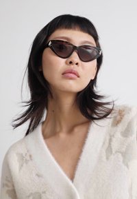 Lunettes de soleil en forme de chat avec des verres teintés foncés et des accents en métal argenté, assorties à un cardigan en tricot blanc avec des motifs d'étoiles beiges.