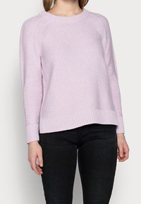 Suéter de punto rosa claro con puños y dobladillo acanalados. Presenta un patrón texturizado y mangas raglán. Combinado con pantalones negros.