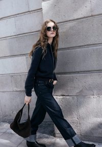 Ciemna bluza z kapturem na zamek, w połączeniu z wysokim stanem dżinsów z podwiniętymi mankietami, czarnymi skórzanymi botkami oraz brązową torebką.