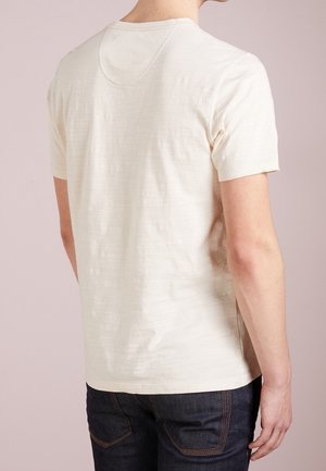 Kremowy, krótki rękaw t-shirt o fakturowanej powierzchni, z okrągłym dekoltem i luźnym krojem, zestawiony z ciemnymi dżinsami.