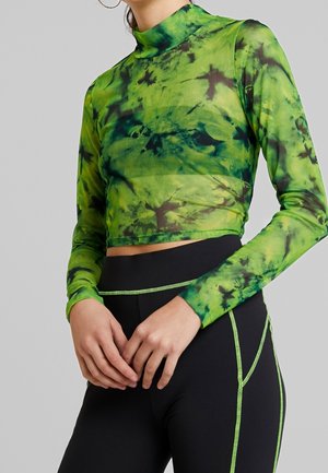 Długi rękaw krótki top w zielony tie-dye z siateczki z czarnymi akcentami, z wysokim kołnierzem. W komplecie czarne legginsy z zielonym przeszyciem.