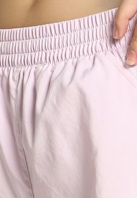 Lyserøde shorts med elastisk talje, glat tekstur og sidelommer, der viser samlet stof for en afslappet pasform.
