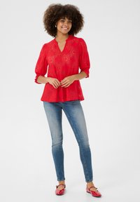 Červený krajkový peplum top s tříčtvrtečními rukávy, kombinovaný s modrými skinny džíny a červenými balerínami. Texturovaný květinový vzor po celém povrchu.