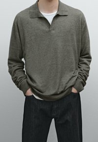 Olijfgroen trui met een kraag, zachte textuur, geribbelde manchetten, gelaagd over een witte T-shirt, gecombineerd met donkerdenim jeans.