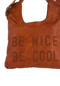 Sac à main en cuir marron avec une surface texturée, ornée du texte imprimé "SOIS SYMPA SOIS COOL" en lettres grasses et foncées sur le devant.