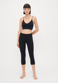 Sutiã desportivo preto e leggings curtas feitas de um tecido elástico com uma textura suave. Cintura com logótipo e design ajustado.