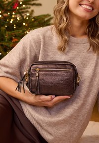 Smeđa metalik torbica za preko ramena s zlatnim detaljima, patentnim zatvaračem i resicama. Mekani, teksturirani kožni materijal. Kompaktni pravokutni oblik.