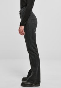 Jeans de mezclilla negra con un corte recto, cintura alta, dos bolsillos traseros y detalles de costura visibles. Combinados con botas de plataforma negras.
