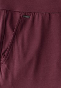 Jogging en tricot bordeaux avec une texture douce, dotés d'une poche sur le côté et d'une petite étiquette métallique au-dessus de la taille.